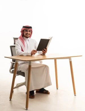 رجل سعودي بالثوب التقليدي يقرأ على مكتب عمل