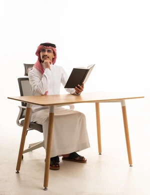 Saudi Man in Traditional Dress Reading at Desk