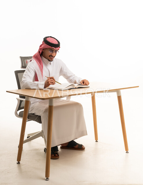 رجل سعودي بالثوب التقليدي يكتب على مكتب عمل