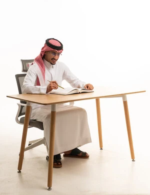 رجل سعودي بالثوب التقليدي يكتب على مكتب عمل