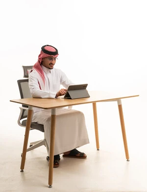رجل سعودي بالثوب التقليدي يعمل على جهاز لوحي