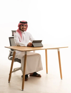 رجل أعمال سعودي على مكتب مع جهاز لوحي بخلفية بيضاء