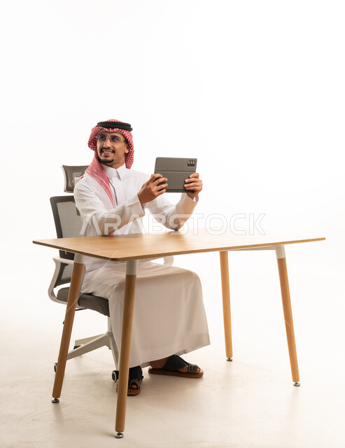 رجل سعودي يرتدي الثوب التقليدي مع جهاز لوحي على مكتب