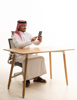 رجل سعودي يستخدم الهاتف الذكي خلف مكتب خشبي
