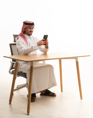 Saudi Man in Traditional Thobe Using Smartphone at Desk