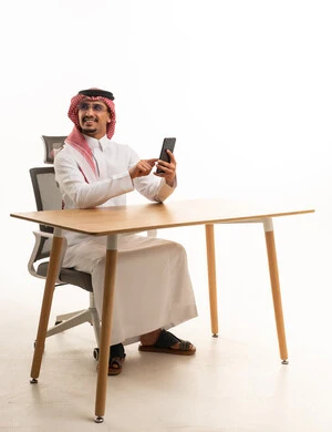 رجل سعودي يستخدم الهاتف الذكي جالسًا في المكتب