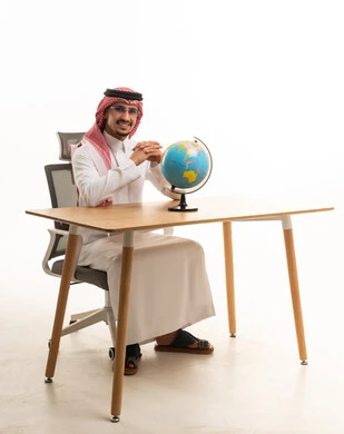 رجل سعودي بالزي التقليدي في مكتب مع كرة أرضية
