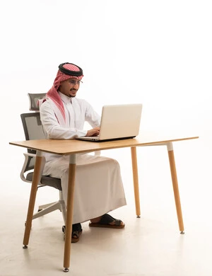 رجل سعودي بالثوب التقليدي يعمل على كمبيوتر محمول