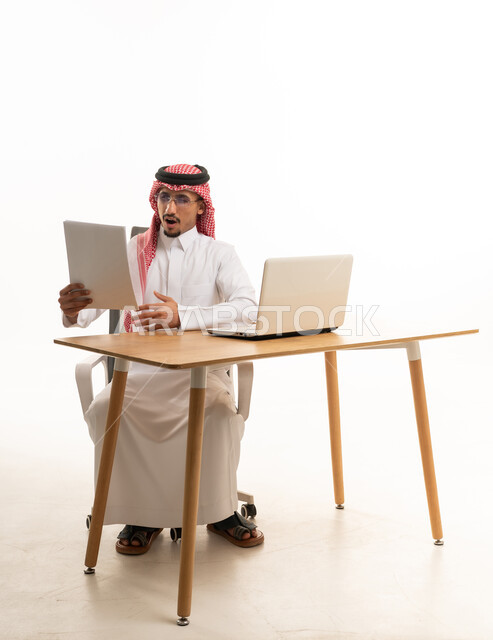 رجل سعودي مندهش ينظر إلى ورقة خلف المكتب