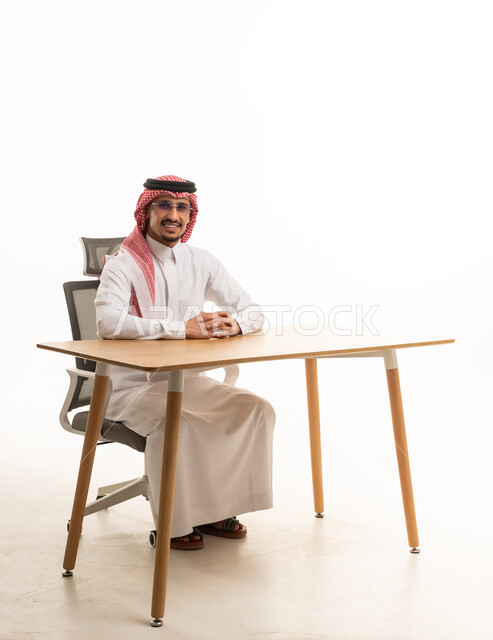 رجل أعمال سعودي يجلس على مكتب عمل خلفية بيضاء