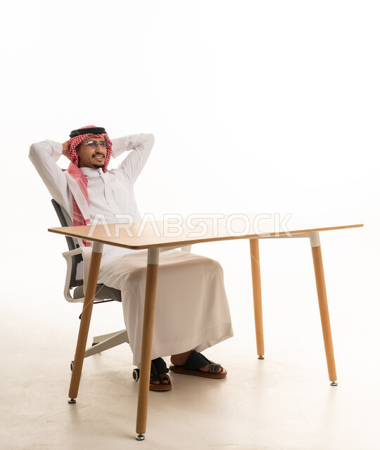 رجل سعودي بالزي التقليدي يسترخي خلف مكتب عمل