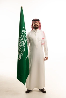 رجل سعودي بالثوب التقليدي يحمل العلم الوطني