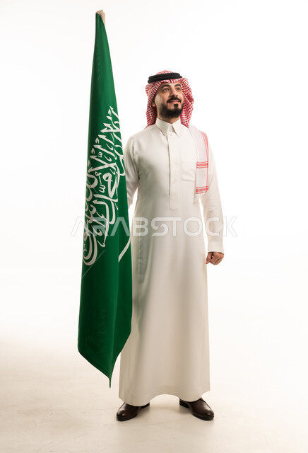 رجل سعودي بالزي التقليدي يقف مع علم السعودية