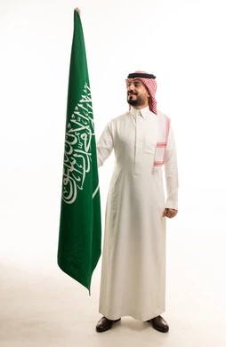 رجل سعودي بالثوب التقليدي يحمل علم السعودية