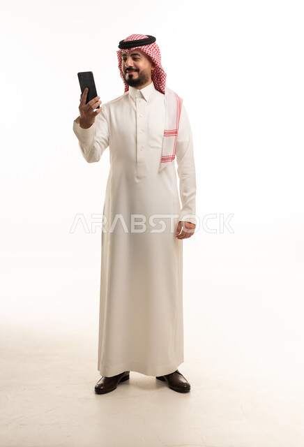 رجل سعودي بالزي التقليدي يستخدم الهاتف الذكي