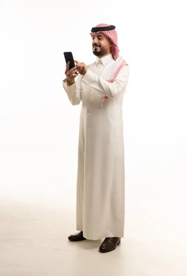 رجل سعودي بالزي التقليدي يستخدم الهاتف على خلفية بيضاء