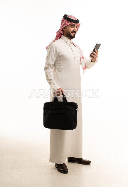 رجل أعمال سعودي مع حقيبة عمل وهاتف ذكي في الاستوديو