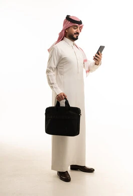 رجل أعمال سعودي مع حقيبة عمل وهاتف ذكي في الاستوديو