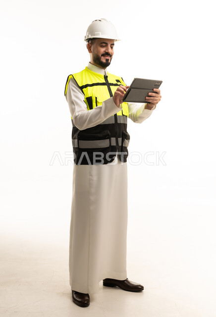 مهندس سعودي بالثوب التقليدي يستخدم جهاز لوحي بخلفية بيضاء