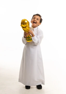 طفل سعودي بالثوب يحمل كأس ذهبي على خلفية بيضاء