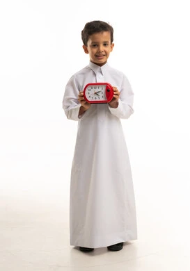 طفل سعودي بالثوب التقليدي يمسك ساعة منبه حمراء