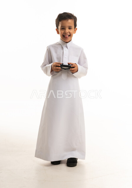 صبي سعودي بالثوب التقليدي يحمل يد تحكم ألعاب