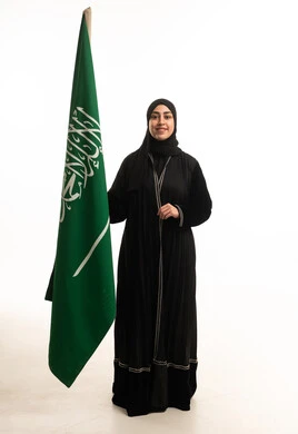 امرأة سعودية بالعباءة تحمل العلم الوطني في استوديو