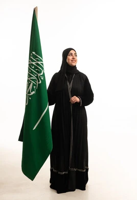 امرأة سعودية بالعباءة مع علم المملكة العربية السعودية