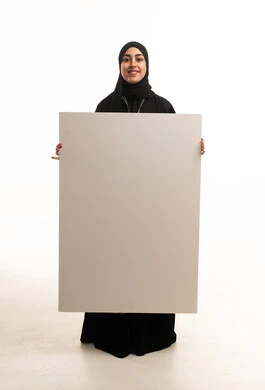 امرأة سعودية تمسك لوحة بيضاء فارغة في استوديو