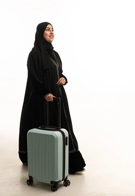امرأة عربية بالعباية تمشي مع حقيبة سفر زرقاء