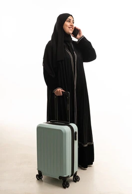 امرأة إماراتية بالعباءة مع حقيبة سفر وهاتف