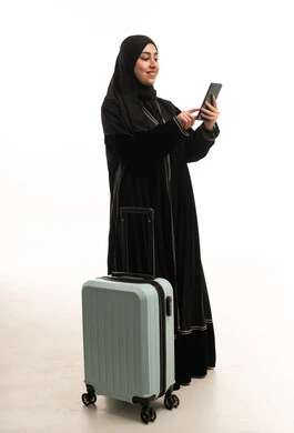 امرأة سعودية بالعباءة مع حقيبة سفر وهاتف ذكي