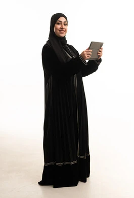 امرأة سعودية بعباءة سوداء تحمل جهازاً لوحياً رقمياً