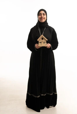 امرأة سعودية تحمل نموذج منزل خشبي على خلفية بيضاء