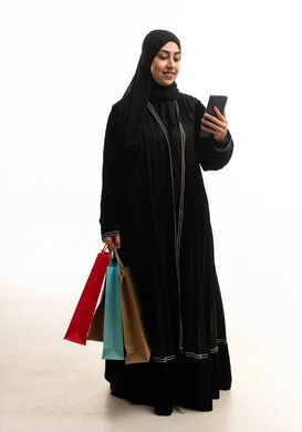 امرأة سعودية مع حقائب تسوق وهاتف ذكي
