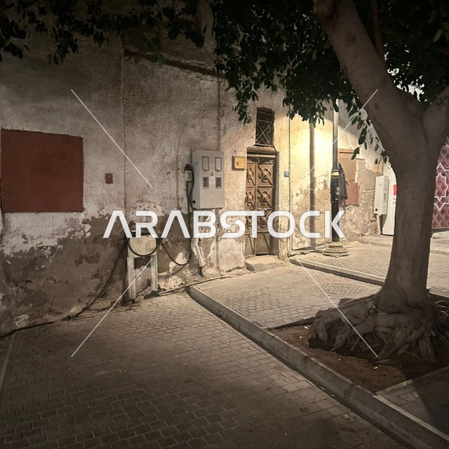 A heritage building made of limestone and old wooden doors in the historic area of Jeddah (Al-Balad). The picture shows details of the dilapidated walls and the stone-paved alley under daylight.