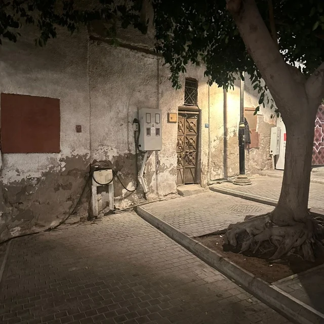 A heritage building made of limestone and old wooden doors in the historic area of Jeddah (Al-Balad). The picture shows details of the dilapidated walls and the stone-paved alley under daylight.