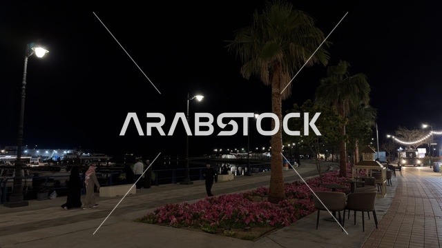 منظر ليلي لفعالية ألوان الجبيل على الممشى البحري في المملكة العربية السعودية. تضيء حبال الزينة الممشى المخصص للمشاة بجانب المباني السكنية الحديثة وأشجار النخيل.