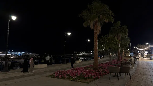 منظر ليلي لفعالية ألوان الجبيل على الممشى البحري في المملكة العربية السعودية. تضيء حبال الزينة الممشى المخصص للمشاة بجانب المباني السكنية الحديثة وأشجار النخيل.