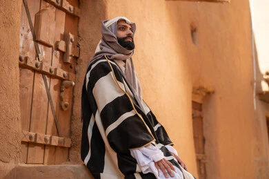 رجل سعودي بالزي التراثي التقليدي أمام بيت طين