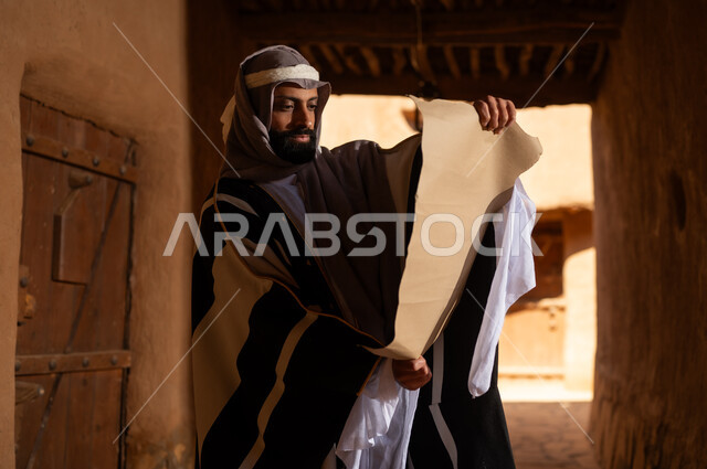 رجل سعودي بالزي التقليدي يقرأ مخطوطة قديمة