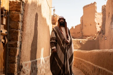 رجل سعودي بالبشت التقليدي في قرية طينية تراثية