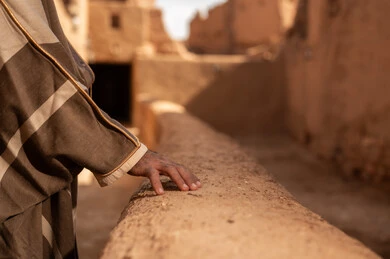 Saudi Man in Traditional Bisht Touching Heritage Mud Wall