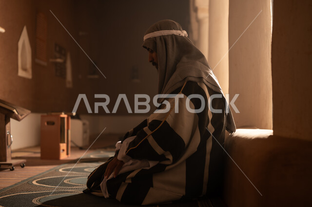 رجل سعودي باللباس التقليدي يصلي في مسجد قديم