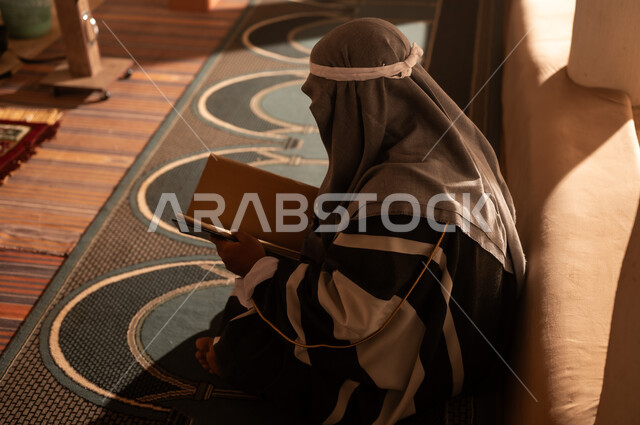رجل سعودي بلباس تراثي يقرأ كتاباً في إضاءة دافئة