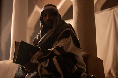 Saudi Man in Historical Attire Holding Book in Clay Building