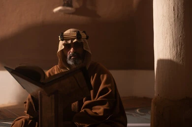 Saudi Man in Traditional Bisht Reading in Clay House