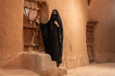 امرأة سعودية بالعباءة في قرية طينية تراثية