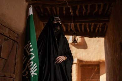 Saudi Woman in Traditional Dress with Flag in Heritage Site