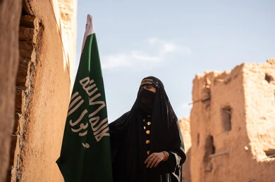 Saudi Woman Holding National Flag in Historic Village